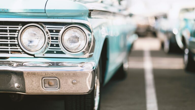 Close-up of a turquoise vintage car's front end with round headlights and chrome grille.
