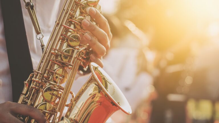Close-up of a musician's hands playing a shiny saxophone with a warm sunset glow in the background lol?